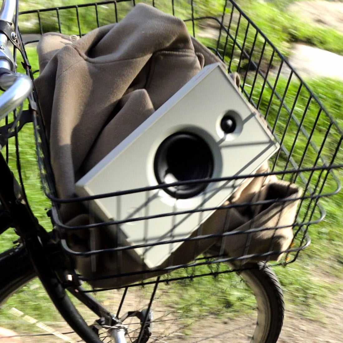 White AIAIAI UNIT-4 MKII speaker carried in the front basket of a moving bicycle