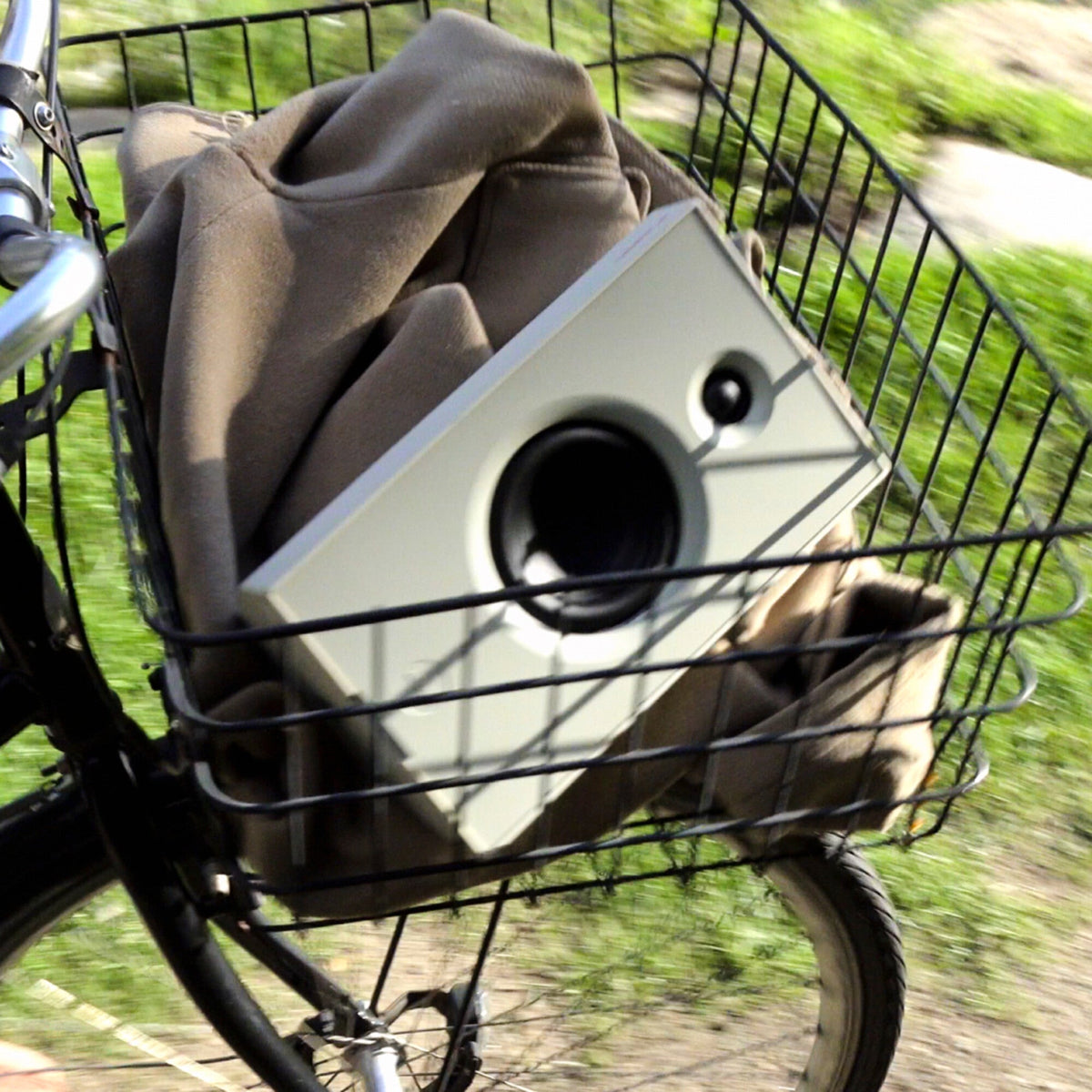 White AIAIAI UNIT-4 MKII speaker carried in the front basket of a moving bicycle