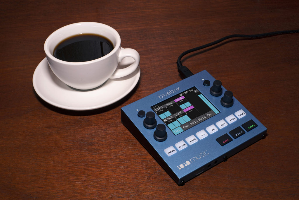 1010music Bluebox digital mixer with colorful knobs and interface, shown in a lifestyle setting with cables and music gear.
