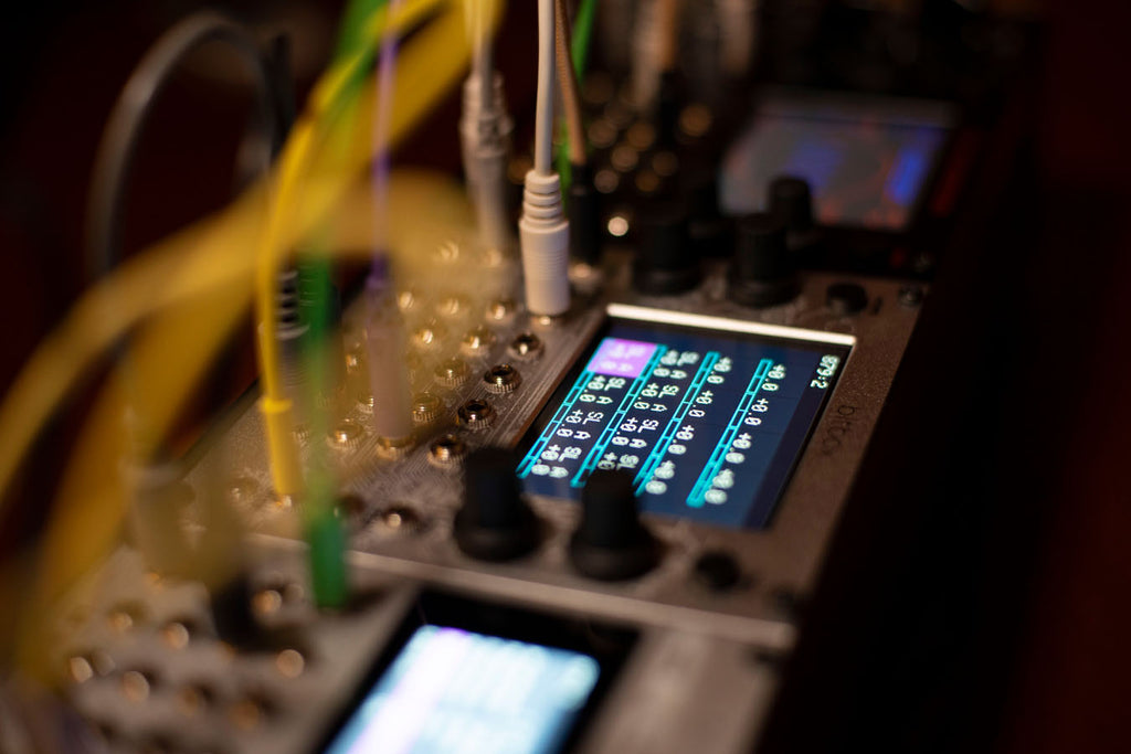 A 1010music Bitbox MK2 semi-modular synthesizer with colorful knobs and patch points, set on a music production desk.