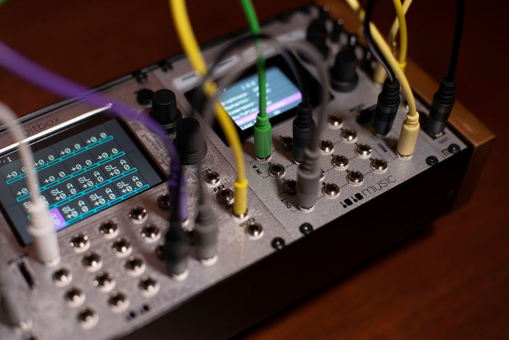 1010music Bitbox Micro semi-modular synthesizer with colorful knobs and patch points, displayed on a music studio setup.