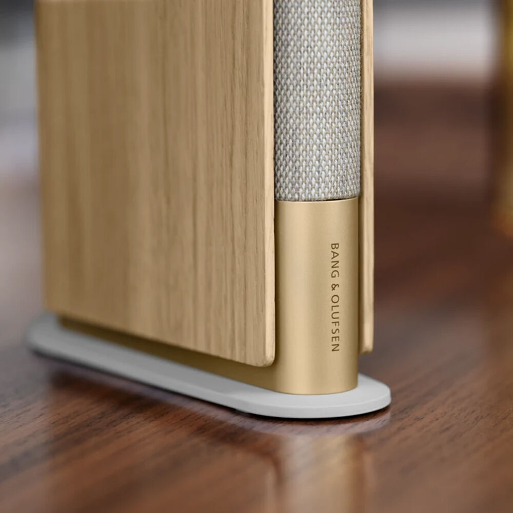 Bang & Olufsen Beosound Emerge wireless speaker in gold tone, featuring a sleek, modern design with fabric grille and smooth finish.