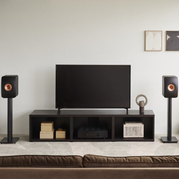 KEF LS50 Meta passive bookshelf speakers in carbon black, shown in a living room setting with sleek modern design