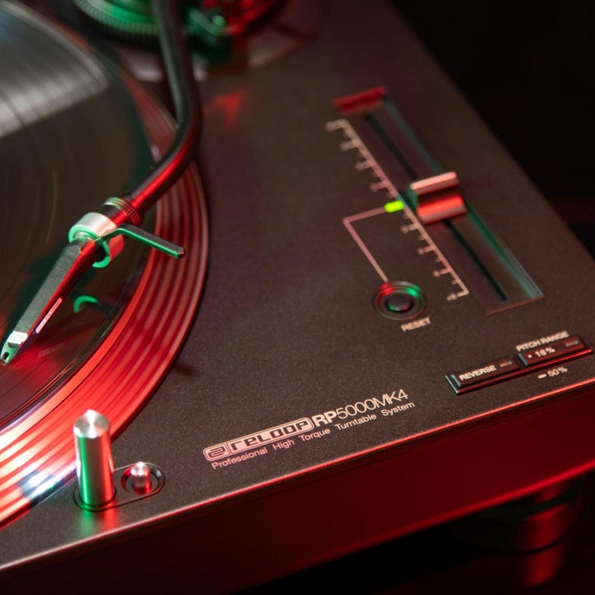 Close-up of Reloop RP-5000 MK4 DJ turntable showing tonearm and platter with detailed controls and branding.