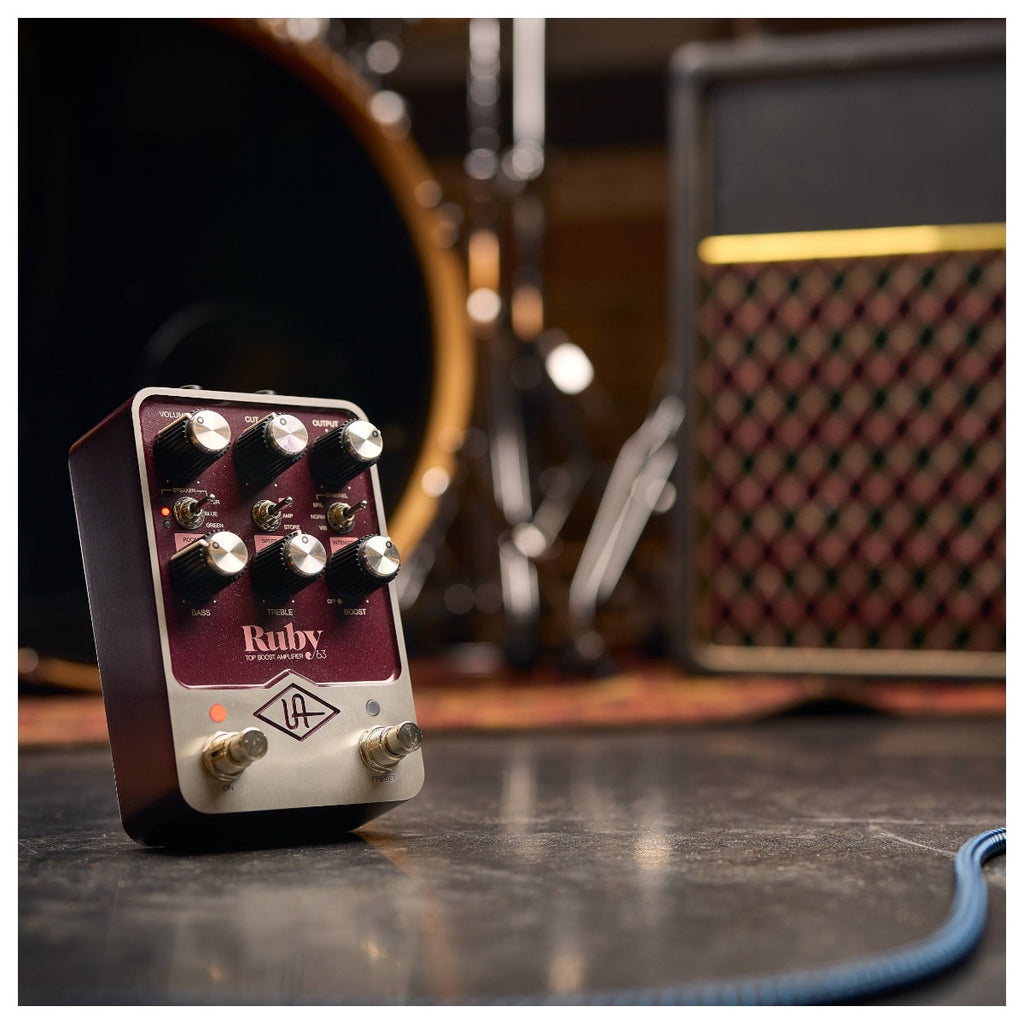 Universal Audio Ruby '63 Top Boost Amplifier on a wooden surface with guitar and cables, showcasing vintage design and controls.
