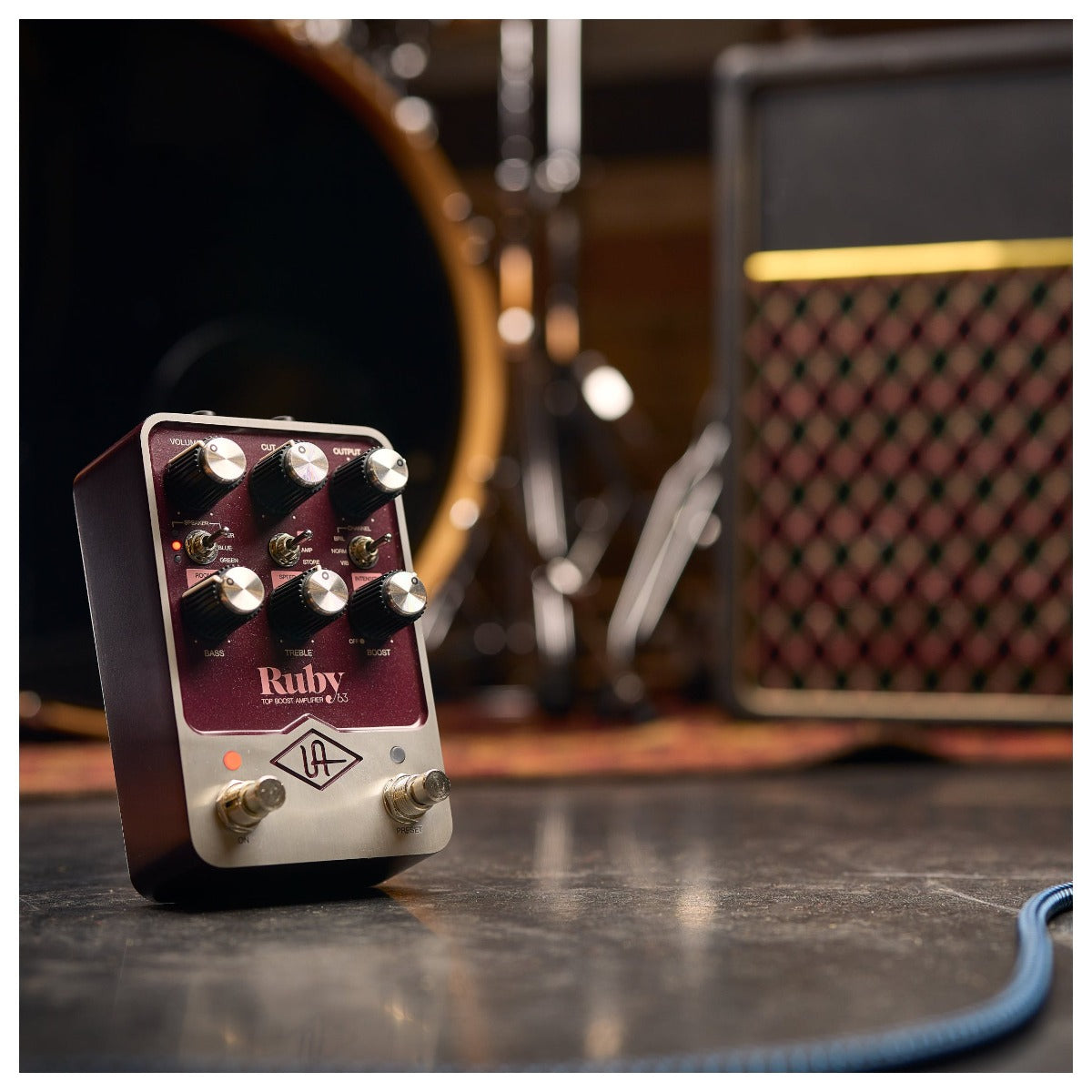 Universal Audio Ruby '63 Top Boost Amplifier on a wooden surface with guitar and cables, showcasing vintage design and controls.
