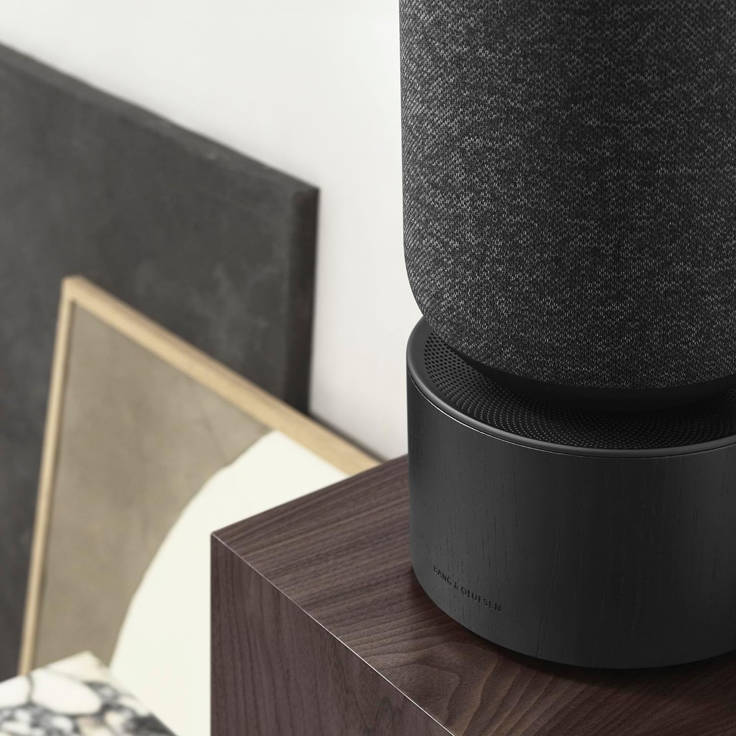Bang & Olufsen Beosound Balance wireless speaker with sleek design and fabric covering, placed on a wooden surface.