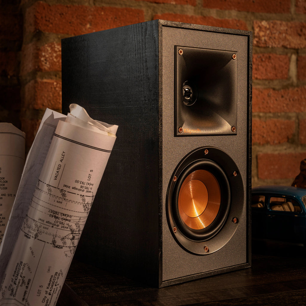 Klipsch R-41PM active bookshelf speakers with wood finish and front ports, positioned on a modern entertainment stand.
