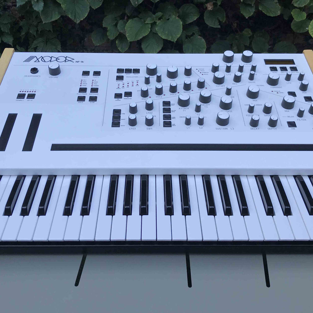 Modor NF-1k keyboard synthesizer with black casing, showing its control knobs and display screen.