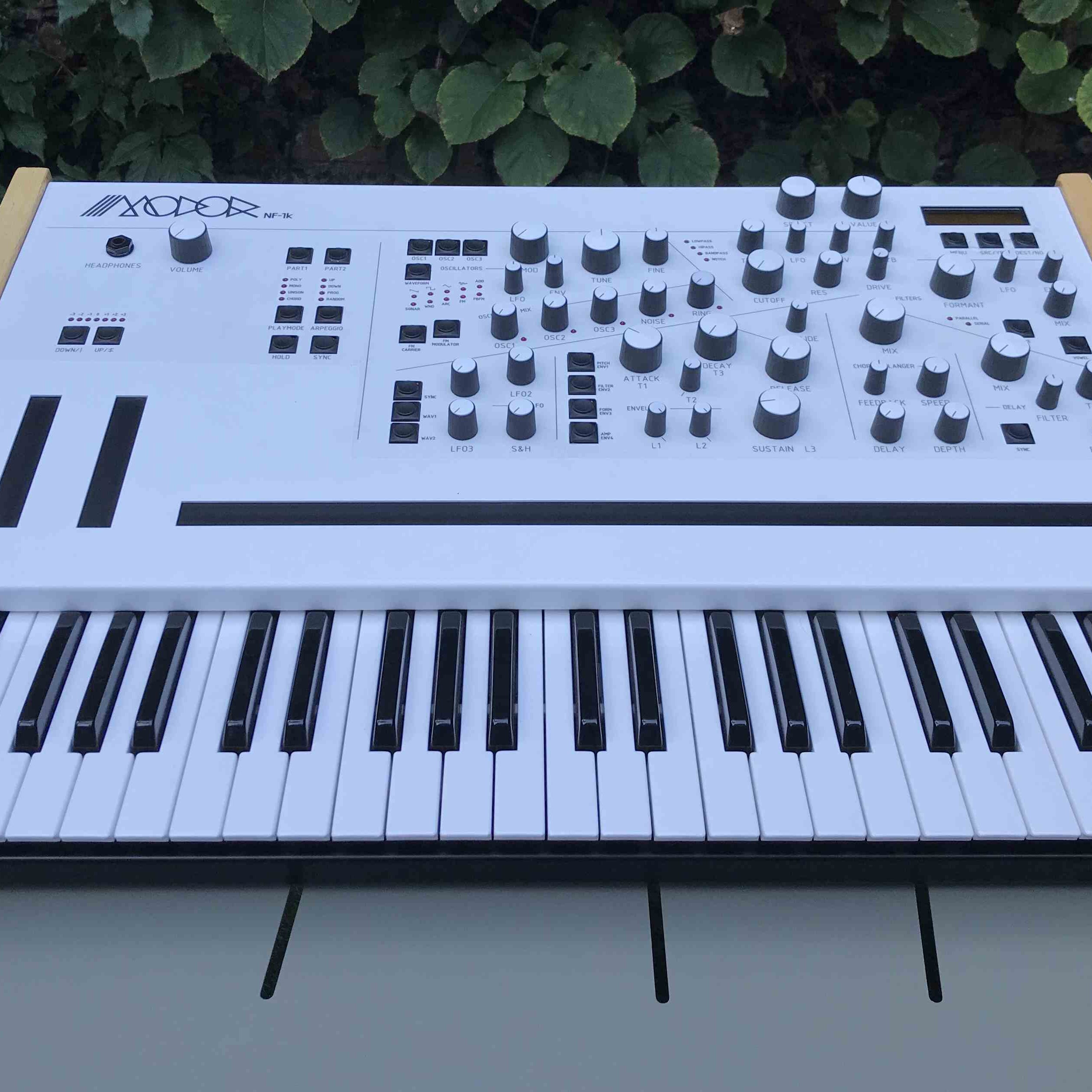 Modor NF-1k keyboard synthesizer with black casing, showing its control knobs and display screen.