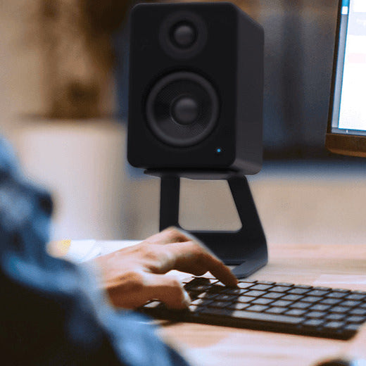 Black Kanto Audio SE2 speaker stands positioned on a desktop, elevating and supporting small speakers in a modern home setup.