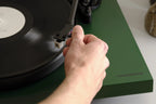 Hand lowering the tonearm onto a record on the Cambridge Audio Spira turntable in Green