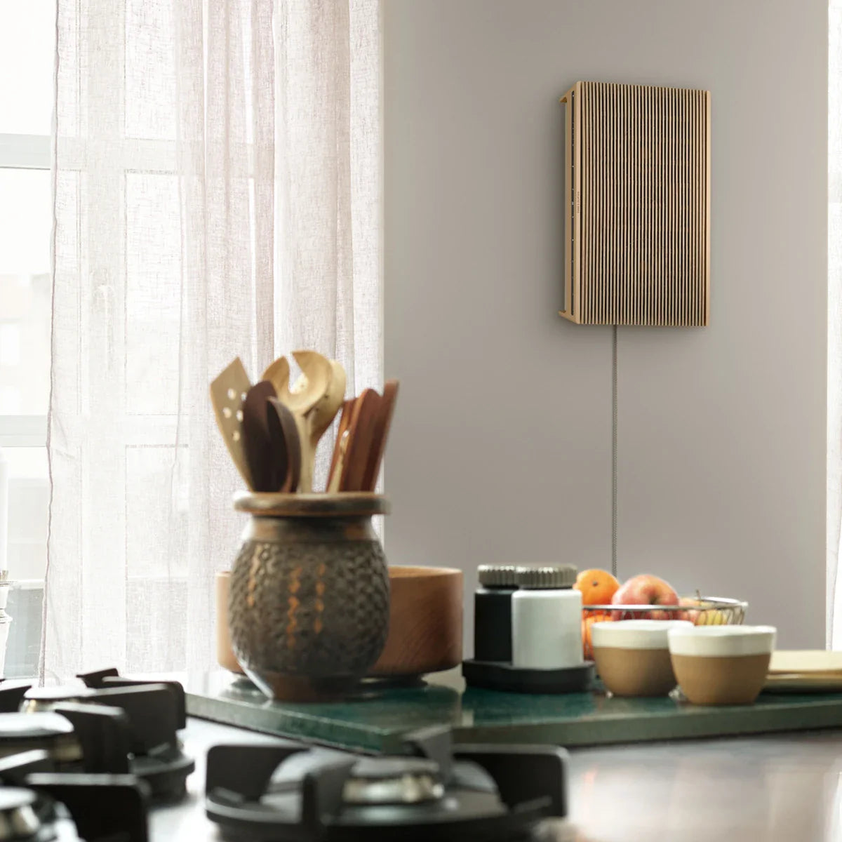 Bang & Olufsen Beosound Level wireless speaker in kitchen with wooden finish, compact and modern design.
