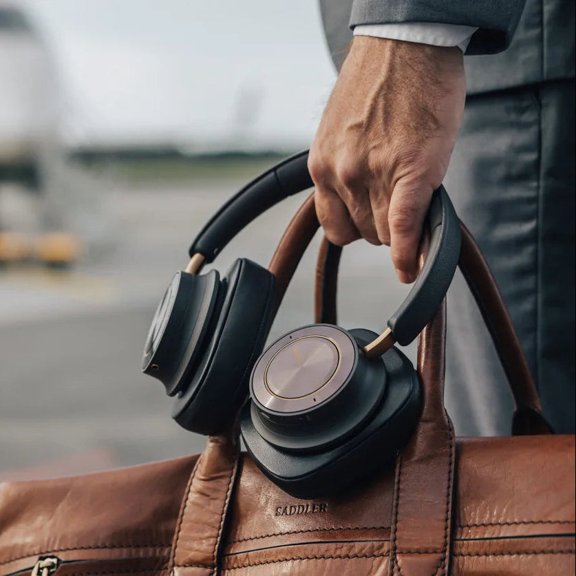 DALI Dali iO-12 wireless headphones resting on a travel bag near an airport gate, showcasing sleek design and portable style.