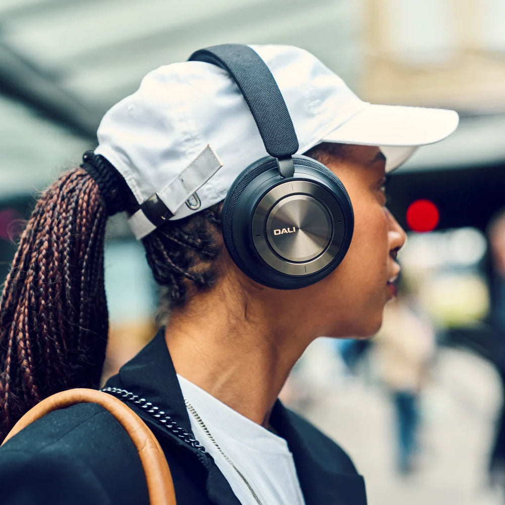 DALI Dali iO-8 wireless headphones worn by a woman on a train, showcasing sleek black ear cups and modern design.