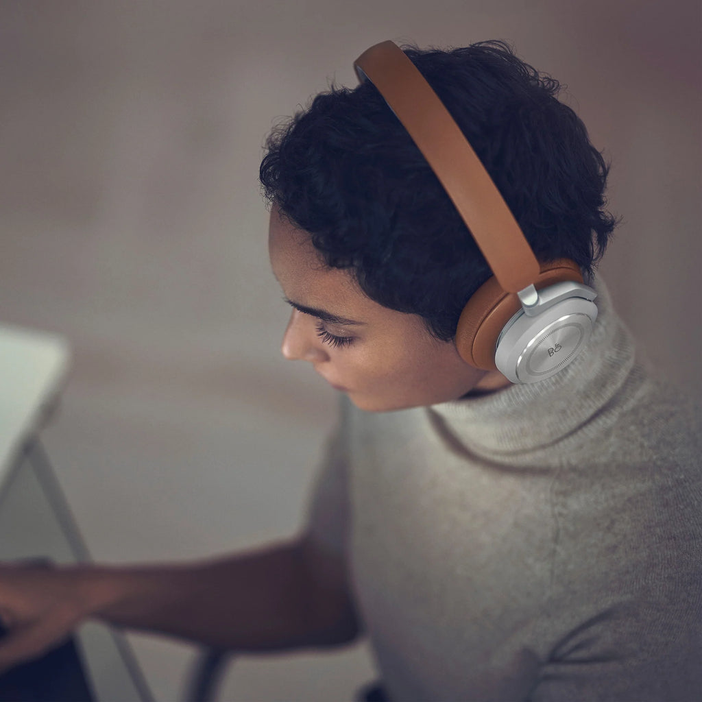 Bang & Olufsen Beoplay HX wireless headphones in timber finish, shown worn in a lifestyle setting with sleek design elements.