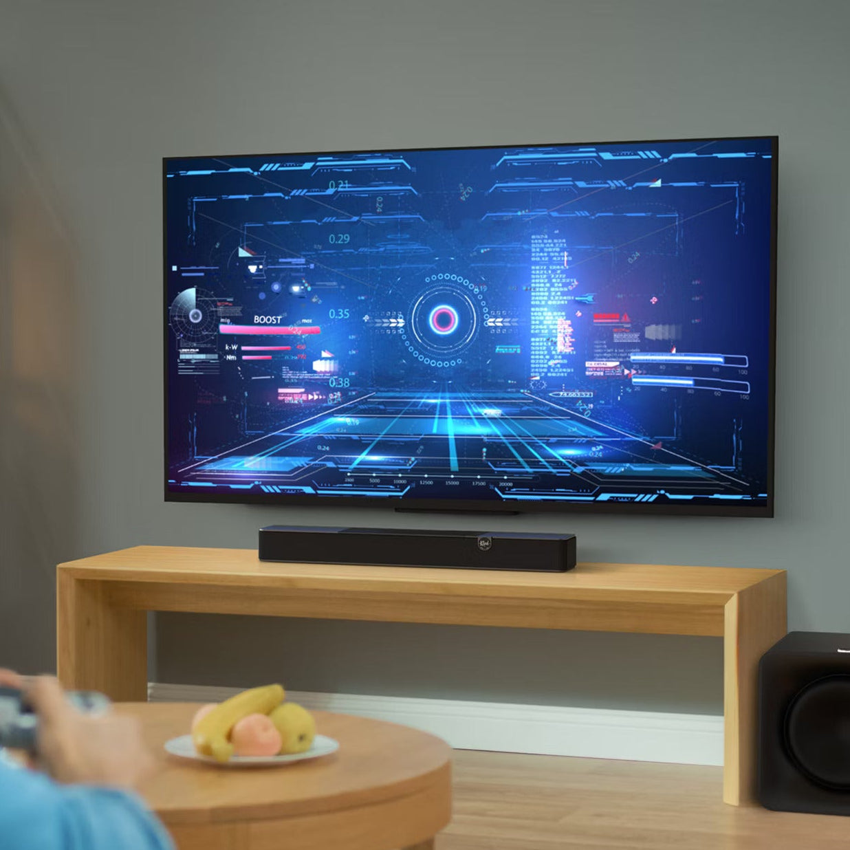 Klipsch Flexus Core 100 soundbar, under wall TV with gaming graphics.