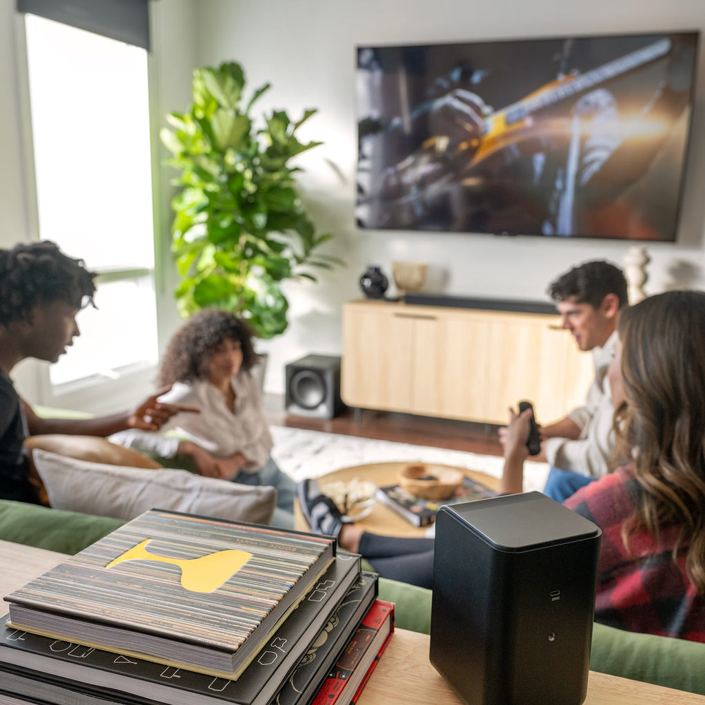Klipsch Flexus SURR 100 soundbar behind friends hanging out, showcasing sleek design and speaker grille for home entertainment.