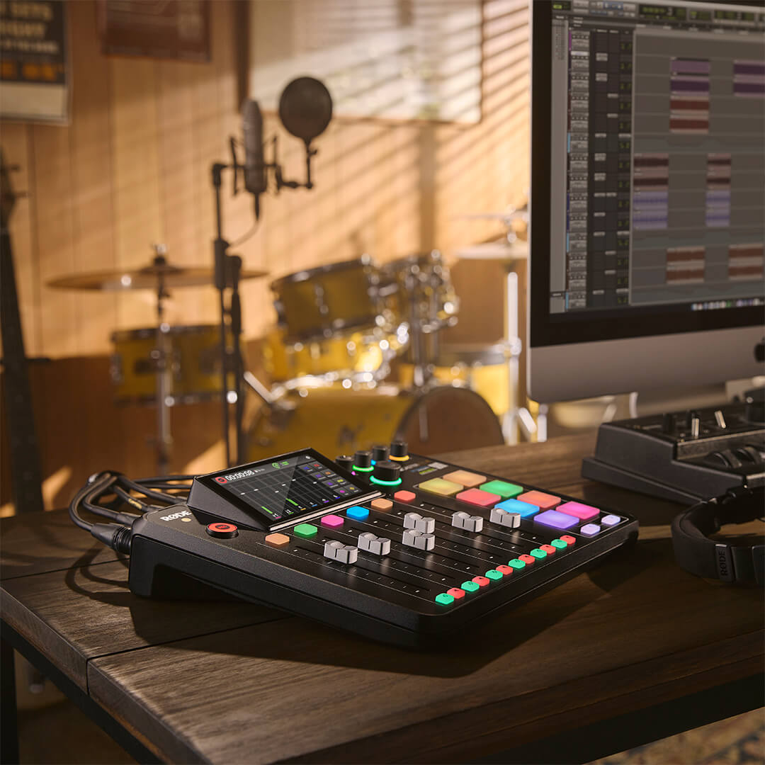 Rode RodeCaster Pro II digital mixer on a table with a musician in a garage setting, showing its control panel and inputs.