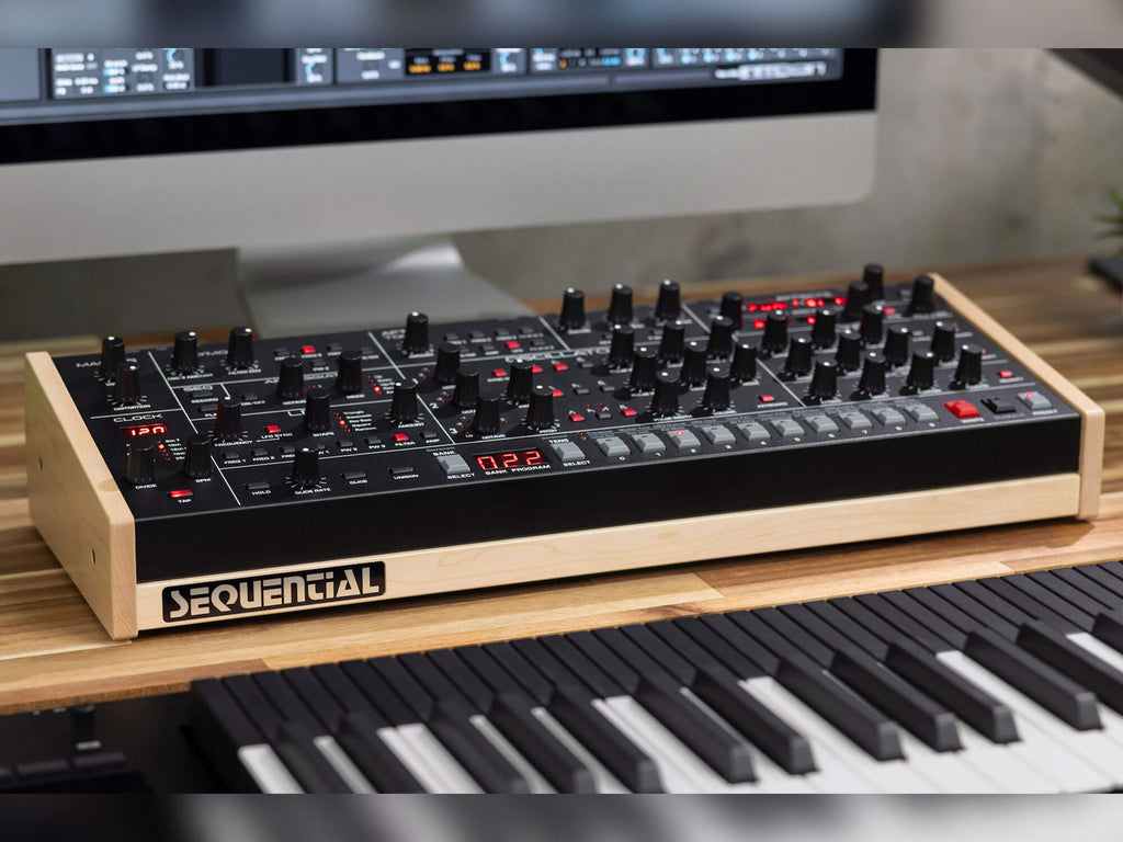 Sequential Trigon-6 desktop synthesizer with black knobs, orange and gray interface, and multiple control buttons on a white background.