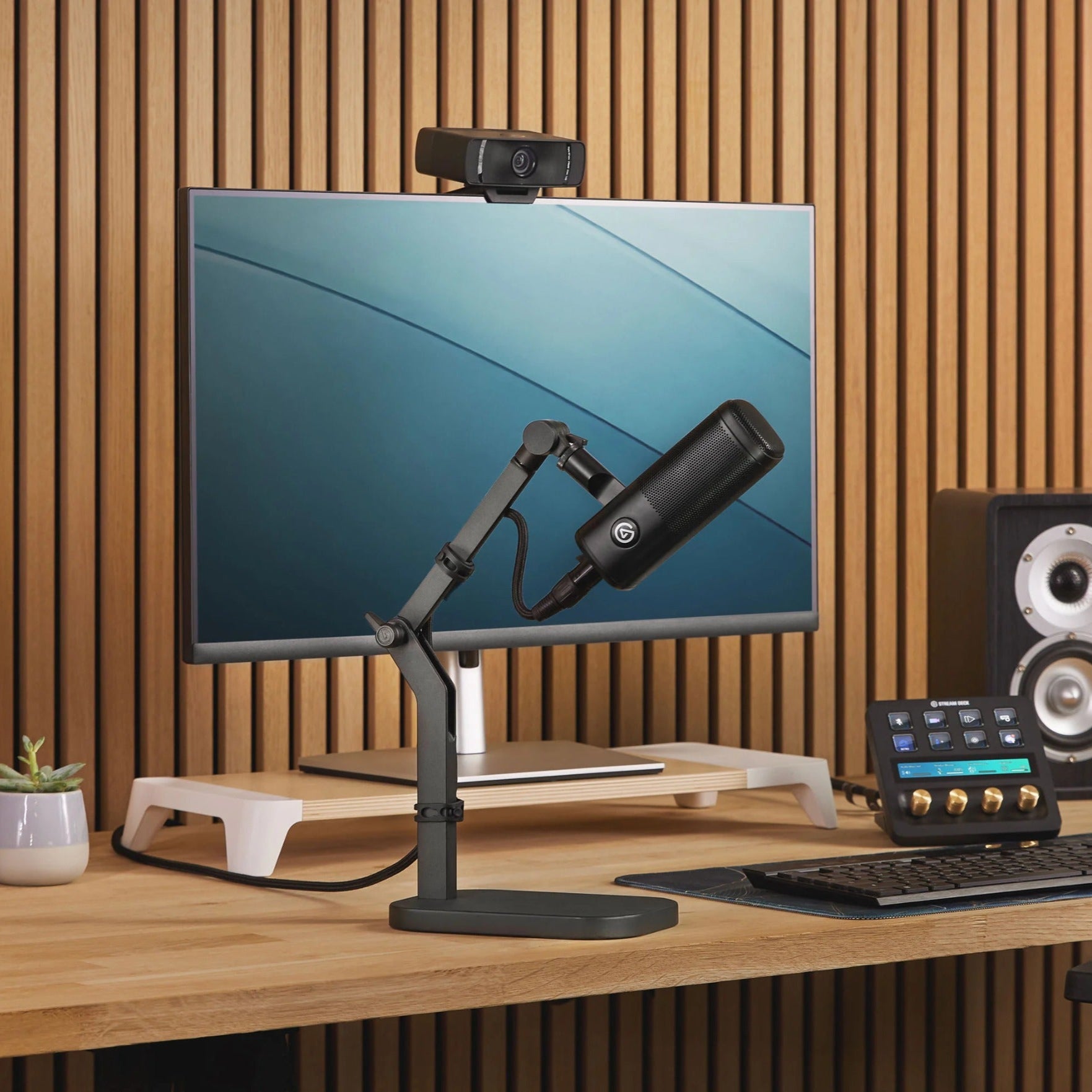 Elgato Wave Desk Stand holding a desktop microphone, shown on a workspace with a laptop and accessories.