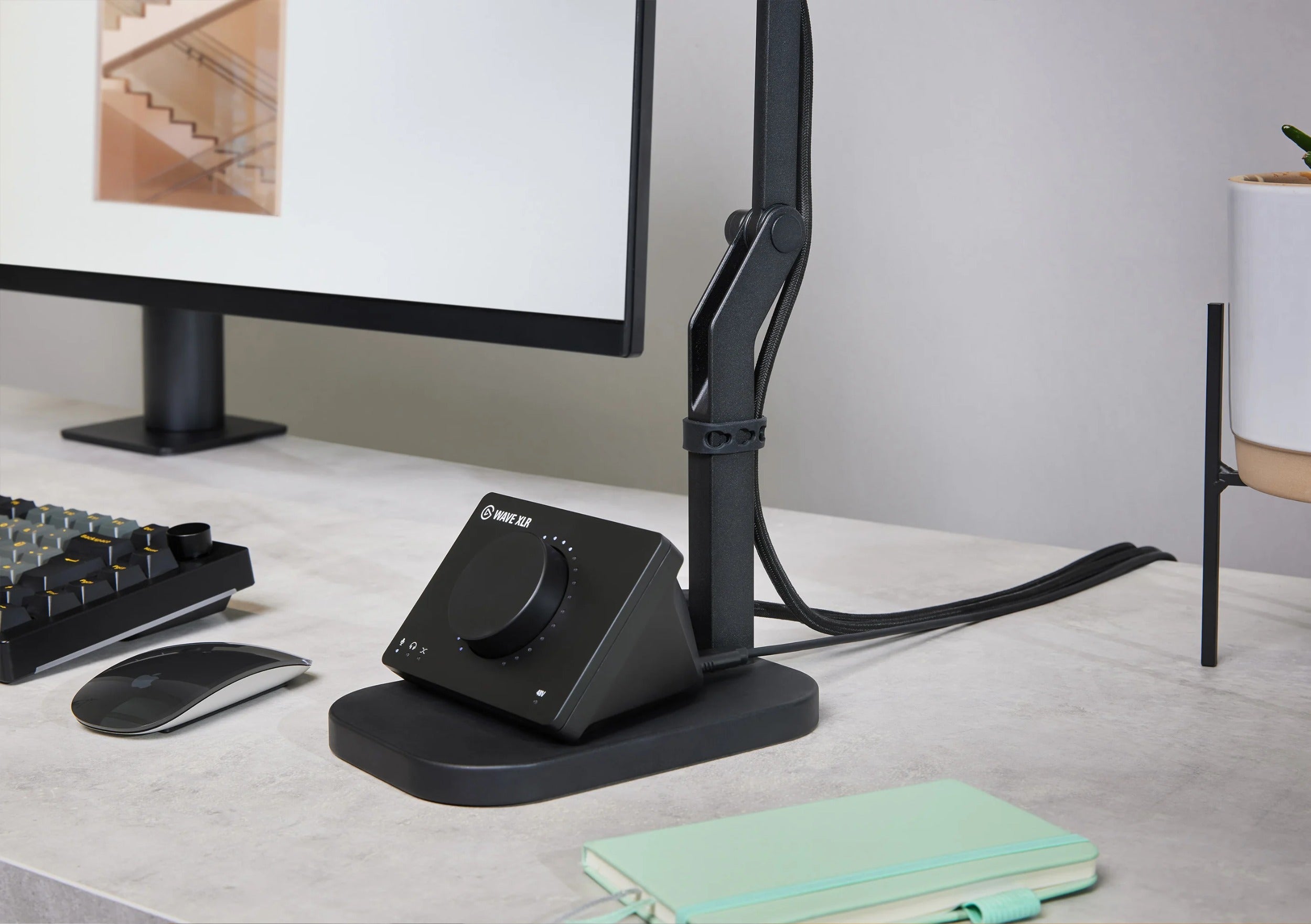 Elgato Wave Desk Stand holding a desktop microphone, shown on a modern workspace with a laptop and accessories.