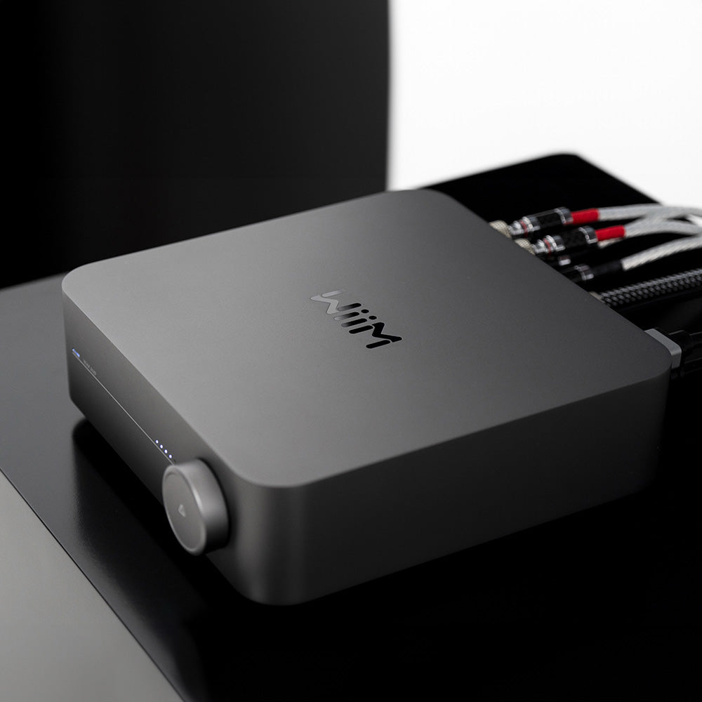 WiiM AMP music streamer displaying a sleek black device with LED indicators and control buttons on a modern home audio setup.